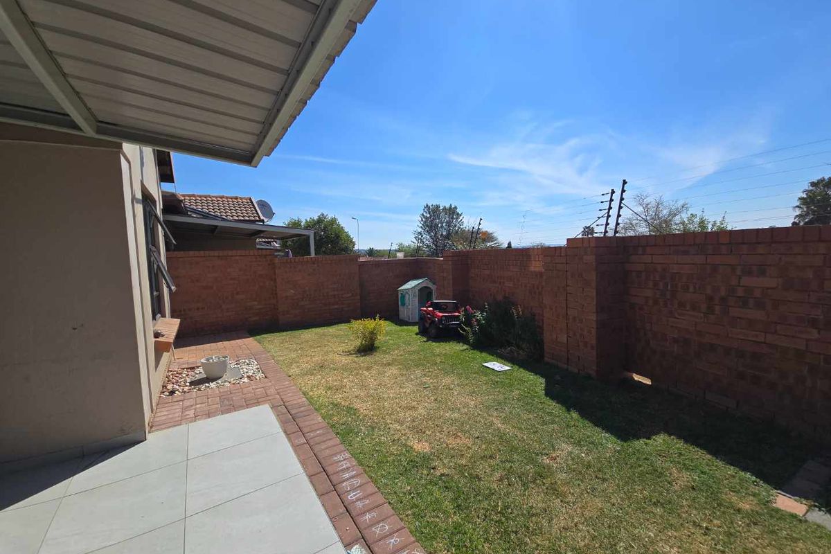 A private rear garden featuring a paved patio area, covered veranda, and high brick boundary walls with electric fencing.