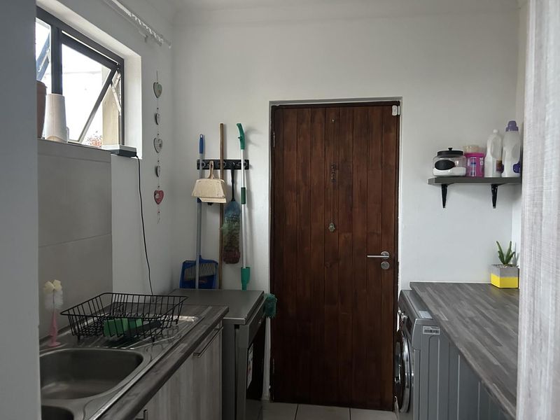 A functional laundry room featuring laminate countertops, a stainless steel sink, tiled flooring, and direct access via a timber door.