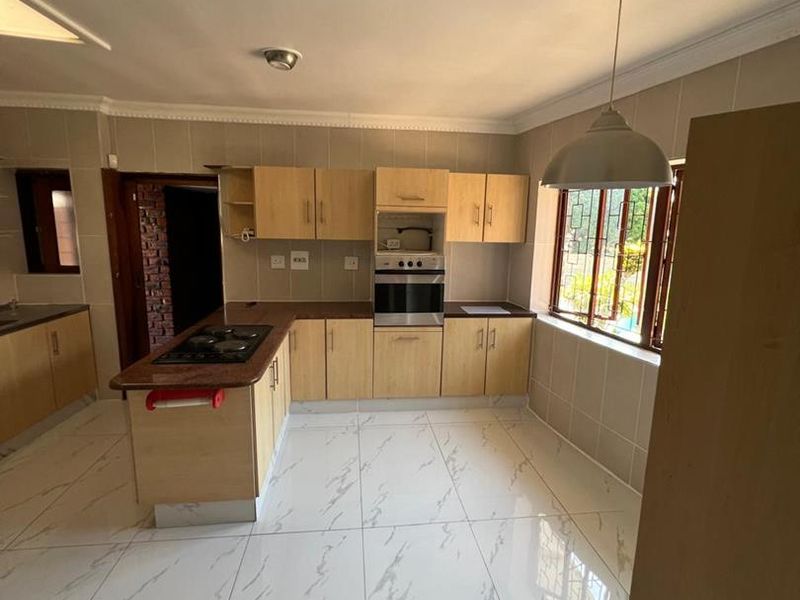 A spacious kitchen featuring light wood cabinetry, built-in oven and hob, tiled flooring, and a neutral tiled backsplash.