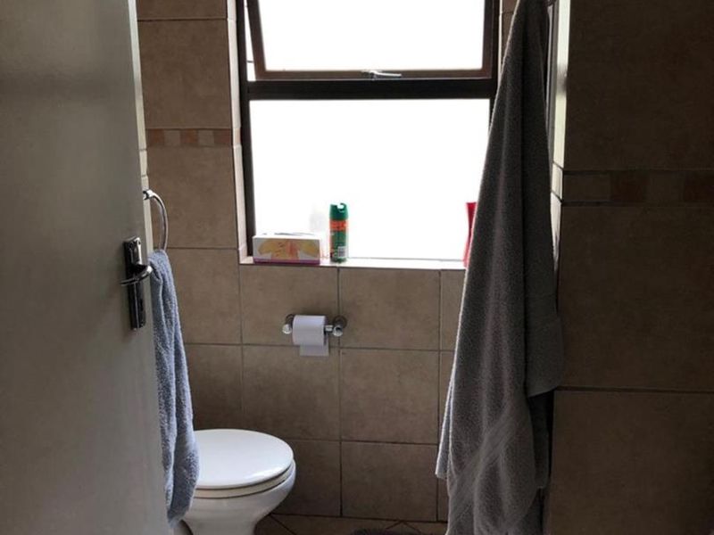 A compact bathroom featuring neutral wall and floor tiling, a standard toilet, and a top-hung window for natural light and ventilation.