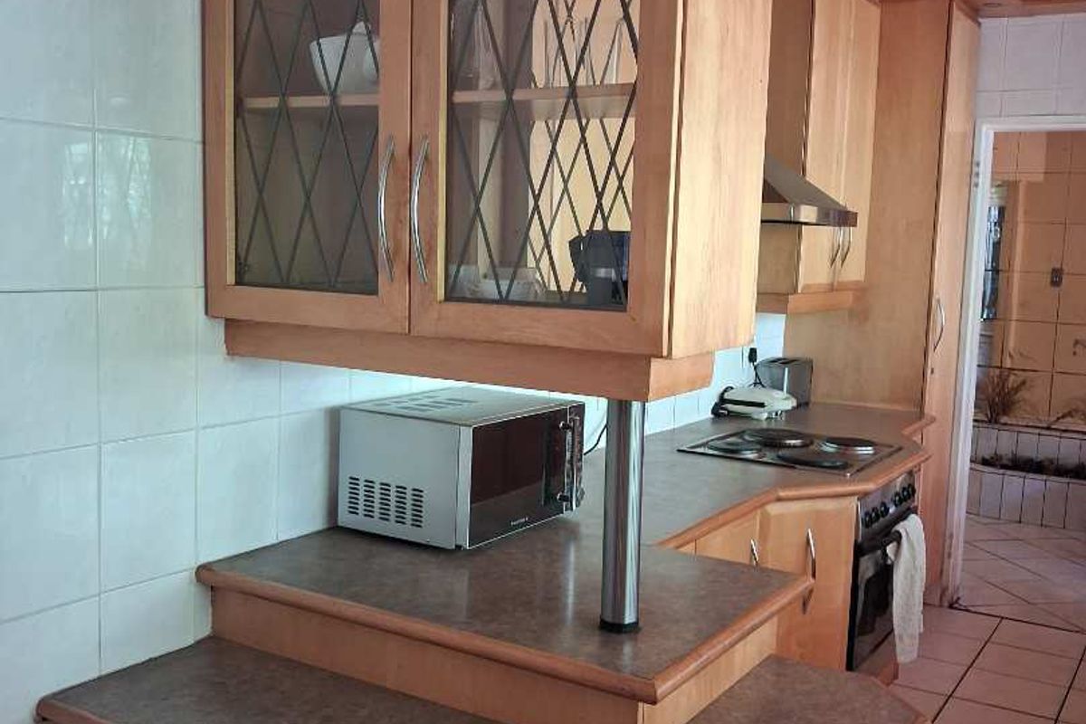 A functional kitchen featuring wooden cabinetry, tiled flooring, a built-in oven, and a hob with an extractor fan.
