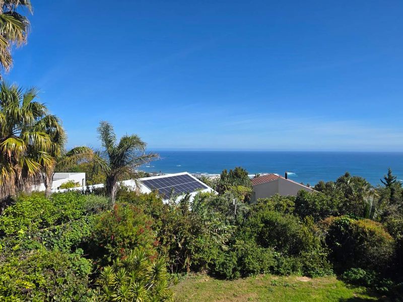A scenic elevated view overlooking the coastline and ocean, featuring lush surrounding vegetation and residential rooftops with installed solar panels.