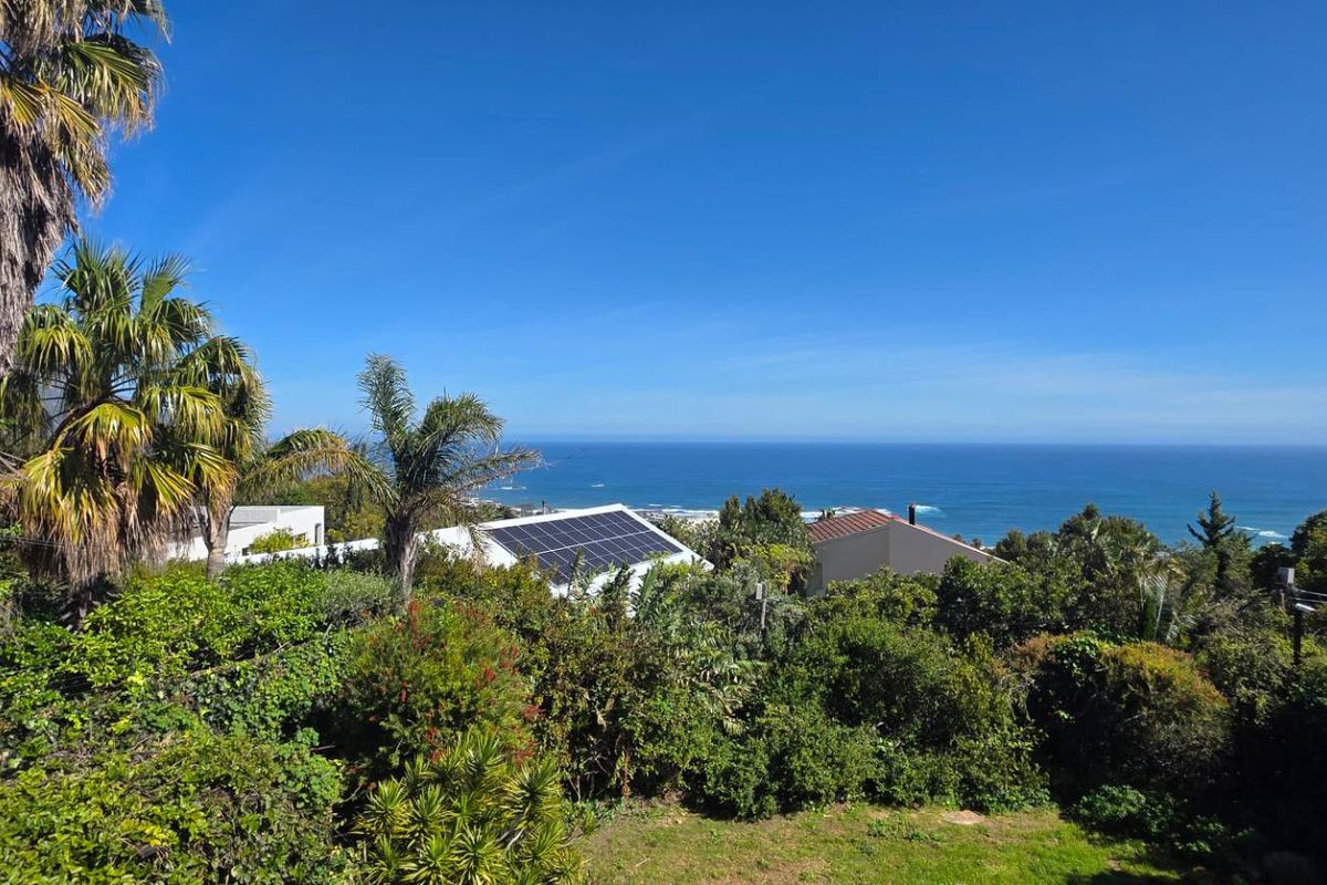 A scenic elevated view overlooking the coastline and ocean, featuring lush surrounding vegetation and residential rooftops with installed solar panels.