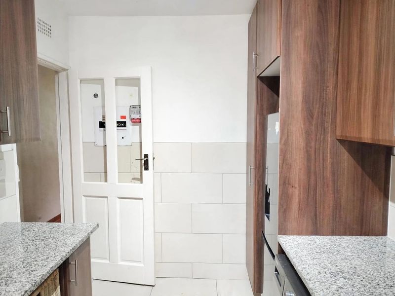 A functional kitchen featuring modern wood-look cabinetry, granite countertops, and neutral tiled splashbacks, providing a clean and practical workspace.