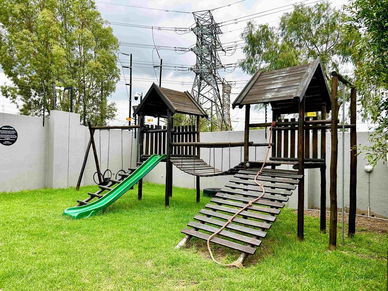 A communal garden area featuring a wooden jungle gym with a slide and climbing ramp, enclosed by a secure perimeter wall.