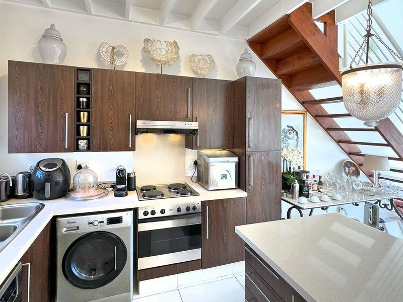Modern kitchen featuring dark wood cabinetry, stone countertops, integrated appliances, and an adjacent wooden staircase with exposed ceiling beams.