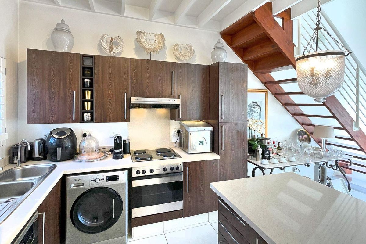 Modern kitchen featuring dark wood cabinetry, stone countertops, integrated appliances, and an adjacent wooden staircase with exposed ceiling beams.