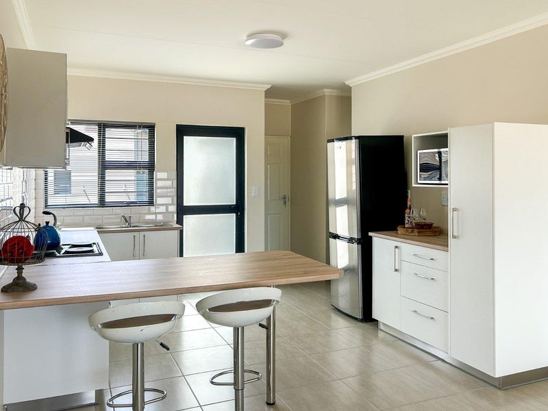 Modern kitchen featuring white cabinetry, wood-look countertops, subway tile backsplash, and integrated appliances with a breakfast bar area.