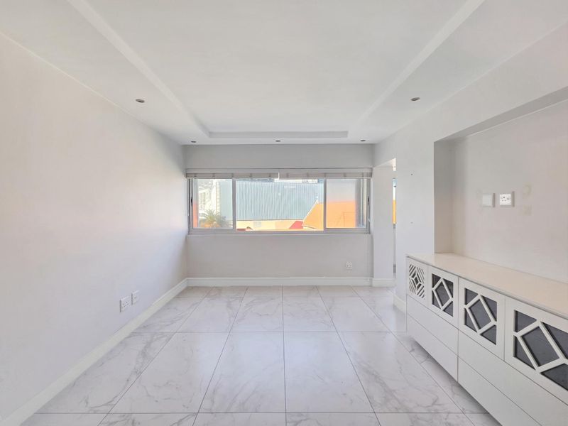 A bright, empty living room featuring modern marble-look floor tiles, recessed ceiling lighting, and built-in white cabinetry.