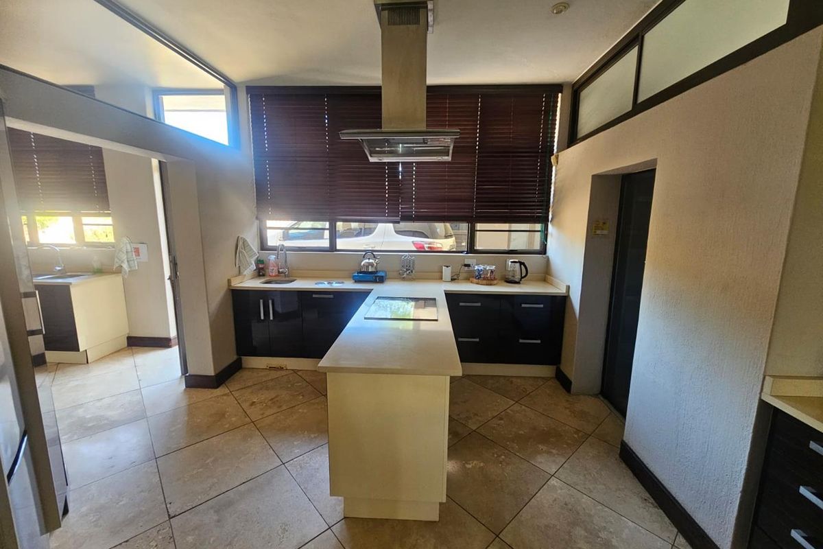 A functional kitchen featuring a central island, dark cabinetry, stone countertops, and a stainless steel extractor fan, with an adjacent scullery area.