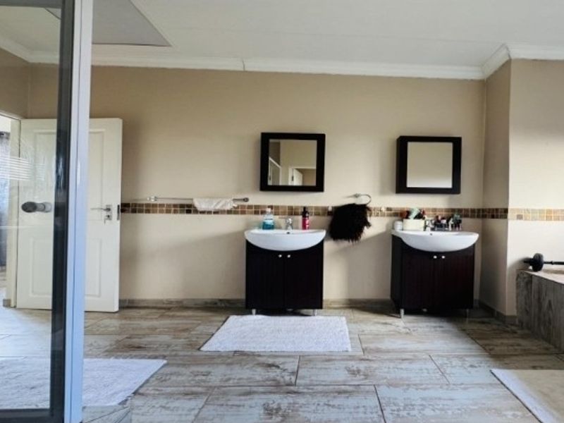 Spacious bathroom featuring a double vanity with dark cabinetry, mosaic tile accents, ceramic floor tiles, and a separate shower and bathtub area.