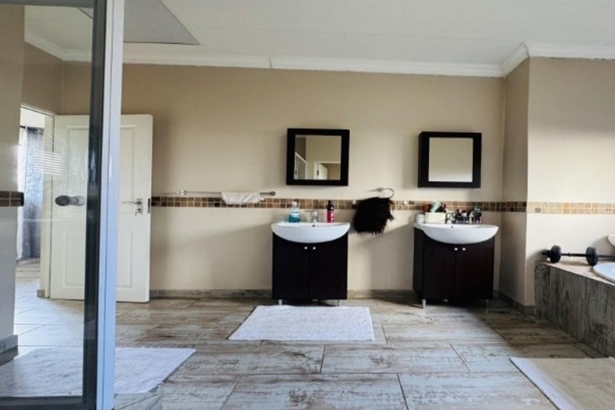 Spacious bathroom featuring a double vanity with dark cabinetry, mosaic tile accents, ceramic floor tiles, and a separate shower and bathtub area.