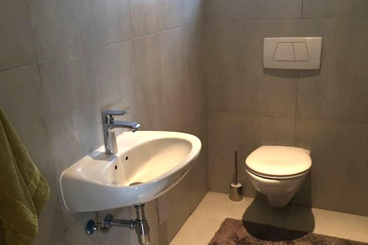 A modern, minimalist bathroom featuring a wall-mounted basin with chrome mixer tap and a wall-hung toilet with a concealed cistern.