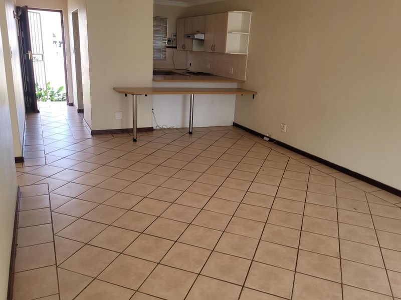 An open-plan living and kitchen area featuring ceramic tile flooring, built-in cabinetry, and a breakfast bar, presented in a vacant, neutral condition.