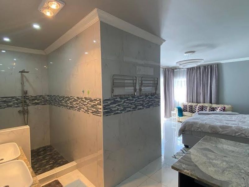 A modern open-plan bedroom featuring an integrated en-suite bathroom with a double vanity, walk-in shower, and contemporary tiled finishes.