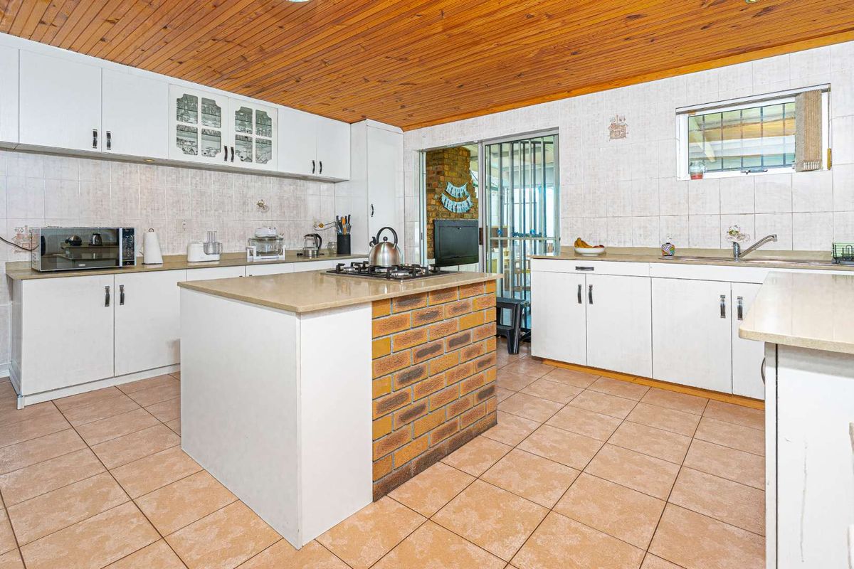 Spacious kitchen featuring a central island with a built-in gas hob, white cabinetry, tiled countertops, and a distinctive wood-paneled ceiling.