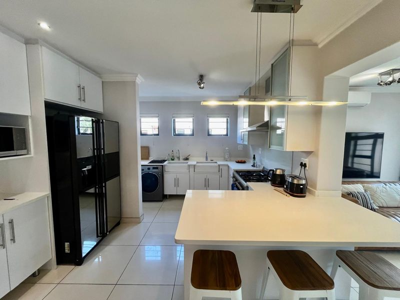 Modern open-plan kitchen featuring white cabinetry, stone countertops, a breakfast bar, and integrated gas hob, seamlessly flowing into the adjacent living area.