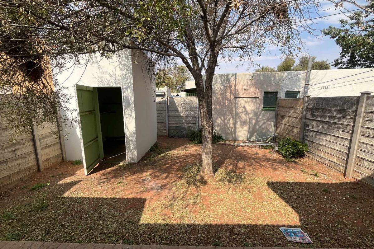A rear courtyard area featuring a small utility outbuilding, enclosed by precast concrete boundary walls and a mature tree.