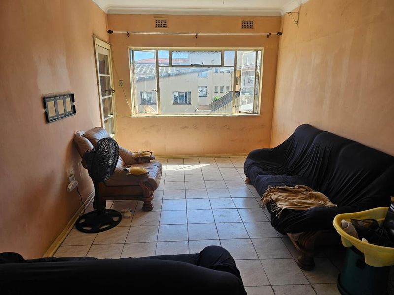 A living room featuring tiled flooring and a large window, currently requiring cosmetic updates to the wall finishes to improve the overall aesthetic.