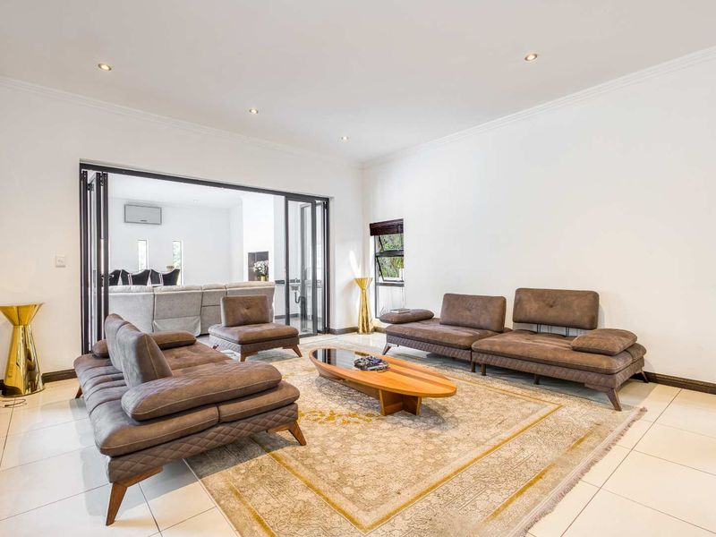 Spacious living room featuring neutral tiled flooring, recessed downlights, and large bi-fold doors providing seamless access to the adjacent living area.