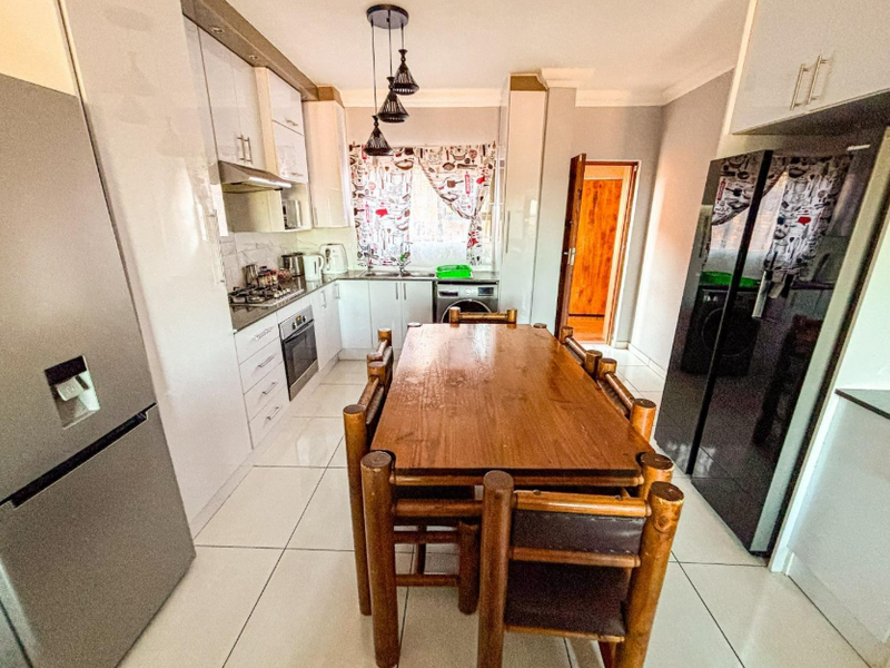 Open-plan kitchen and dining area featuring modern white cabinetry, gas hob, electric oven, and polished floor tiles.