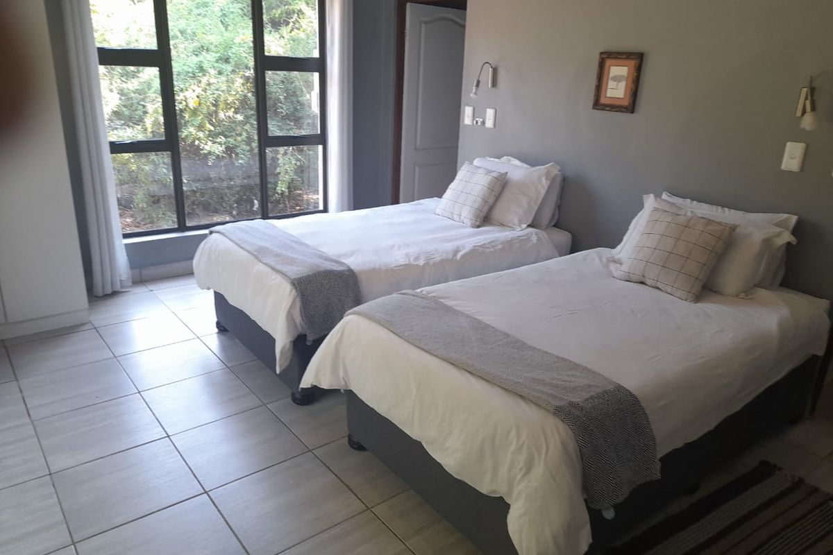 A spacious bedroom featuring large windows, neutral grey walls, and light-colored floor tiles, offering a bright and functional living space.