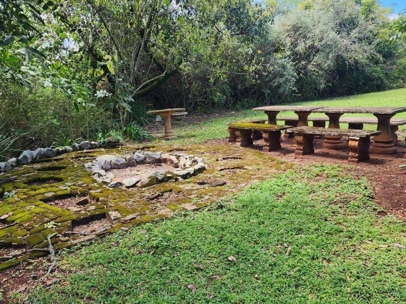 Outdoor garden area featuring a stone fire pit, brick paved section, and fixed stone bench seating set within a natural landscape.