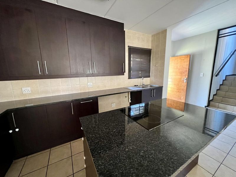 Functional kitchen featuring dark wood cabinetry, granite countertops, built-in electric hob, and tiled finishes, adjacent to an internal staircase.