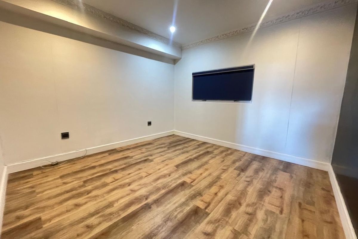 A clean, empty bedroom featuring modern laminate flooring, recessed downlighting, and decorative cornice detailing, providing a versatile blank canvas for interior design.
