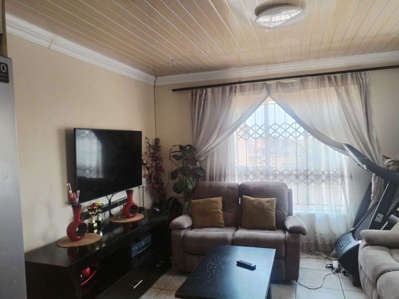 A comfortable living room featuring tiled flooring, a timber panelled ceiling, and a window fitted with a security gate.