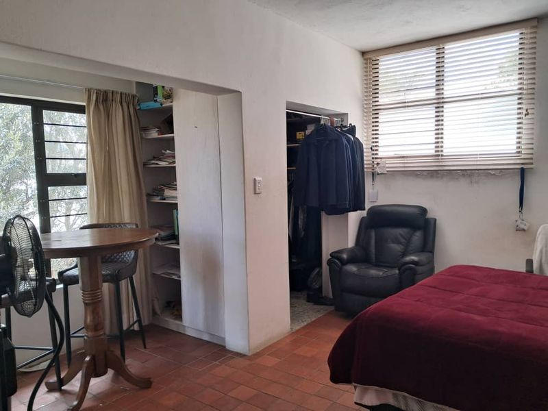 Bedroom featuring terracotta tile flooring, built-in shelving, and a built-in closet, with natural light provided by a large window with venetian blinds.