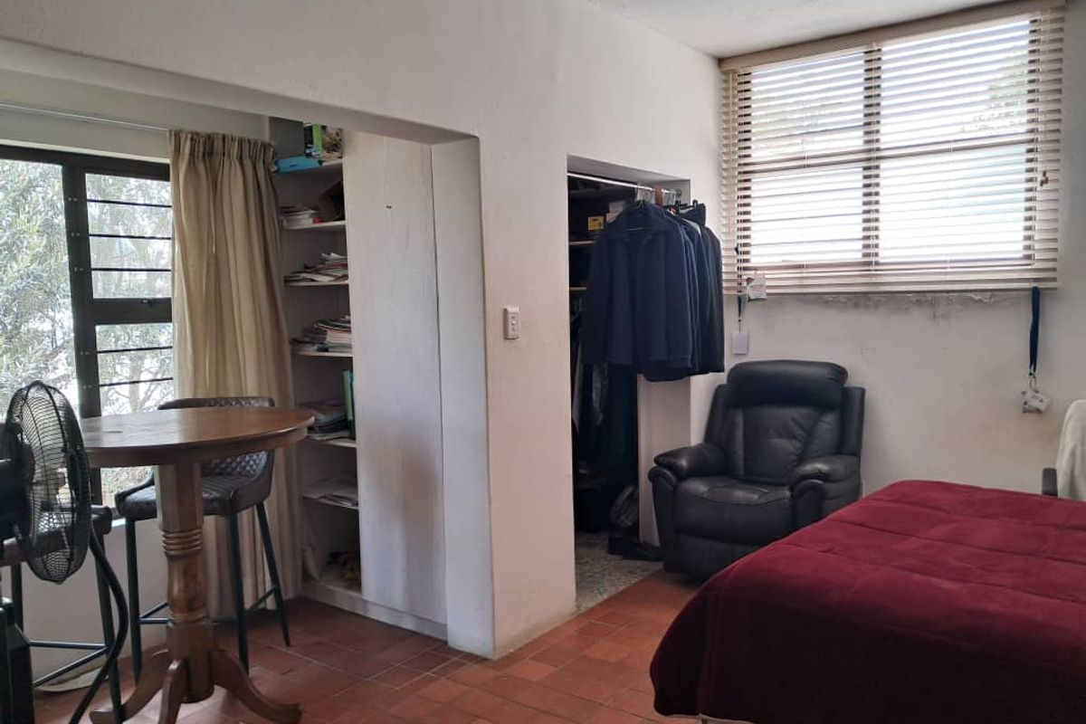 Bedroom featuring terracotta tile flooring, built-in shelving, and a built-in closet, with natural light provided by a large window with venetian blinds.