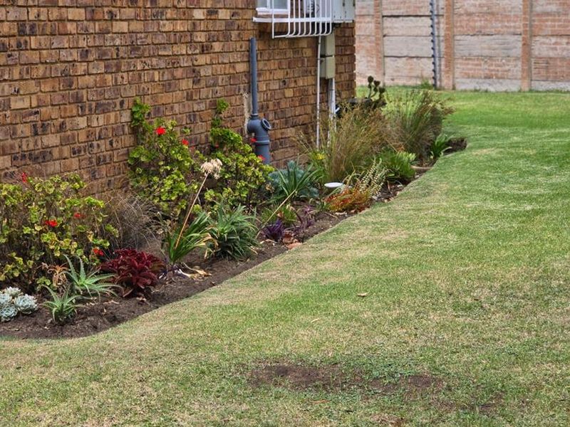 A side view of the townhouse exterior featuring a brick facade, security window bars, a solar panel installation, and a landscaped garden bed.