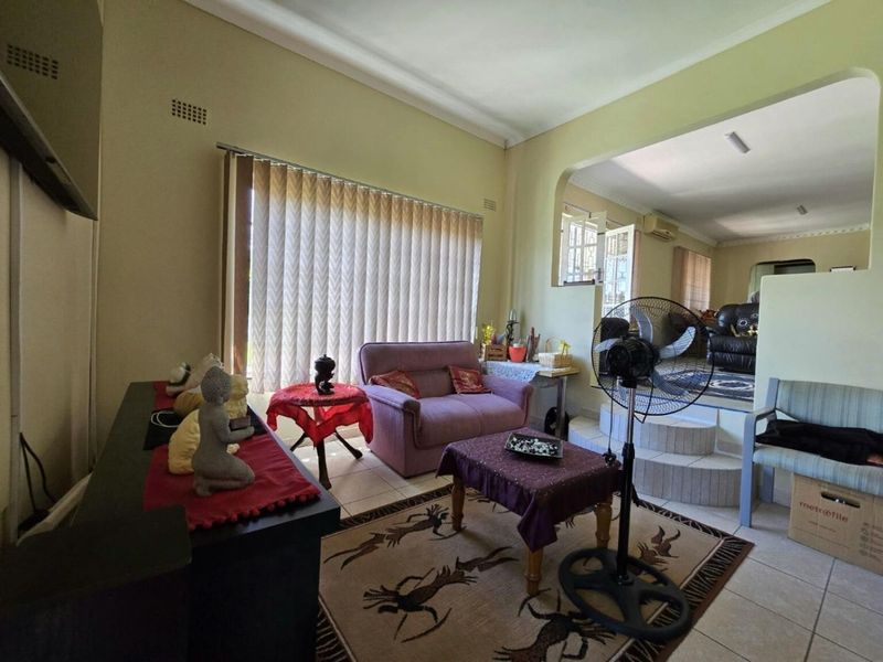 A living room featuring tiled flooring, an arched opening leading to an adjacent space, and vertical blinds on the window.