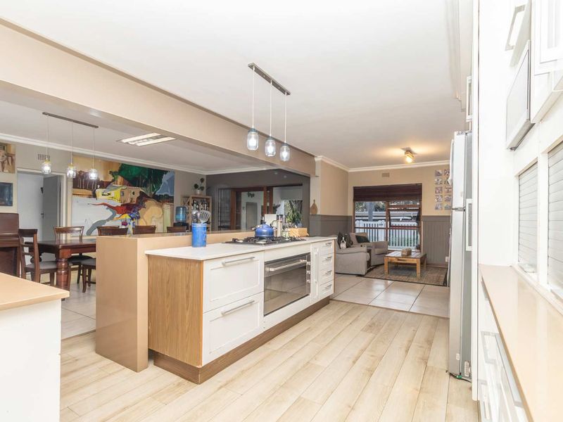 Spacious open-plan kitchen and living area featuring a central island with built-in oven and hob, flowing into a dining and lounge space.