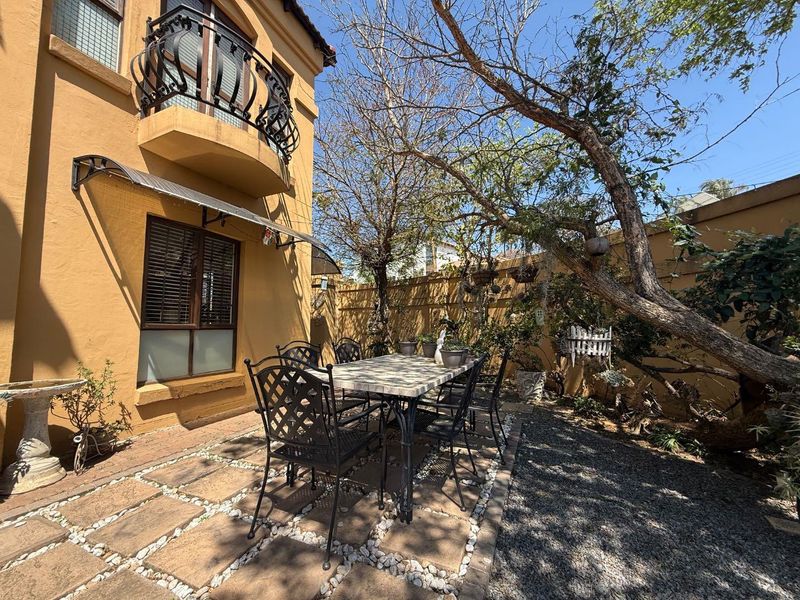 A private rear courtyard featuring a paved patio area, established trees, and a balcony overlooking the garden space.