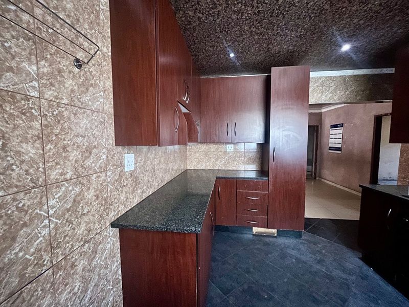 A functional kitchen featuring dark wood cabinetry, granite countertops, and tiled finishes, offering a clean, empty space ready for personalization.
