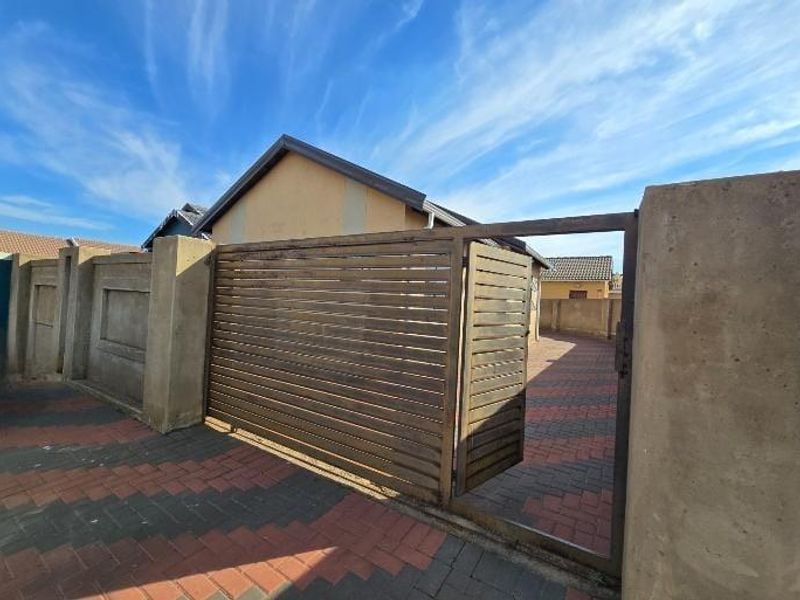 Front exterior view featuring a paved driveway, secure perimeter wall, and a sliding gate providing access to the property.