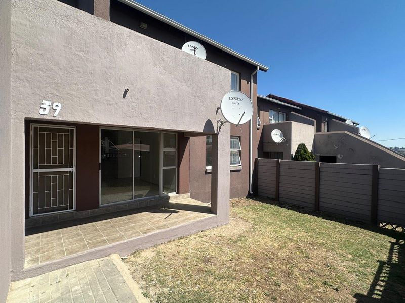 Rear view of the apartment featuring a covered tiled patio, sliding glass door with security gate, and a private garden area with boundary wall.