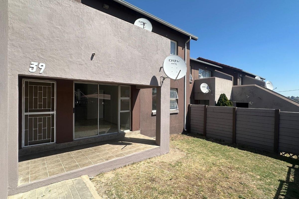 Rear view of the apartment featuring a covered tiled patio, sliding glass door with security gate, and a private garden area with boundary wall.