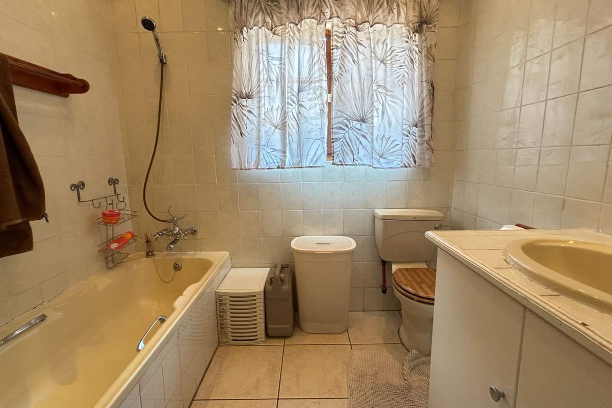 A functional bathroom featuring a bathtub with shower mixer, toilet, and vanity basin, finished with tiled walls and flooring.