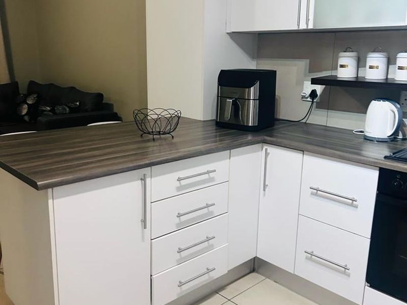 A modern kitchen featuring white cabinetry, dark laminate countertops, built-in oven, and tiled flooring, offering a clean and functional workspace.