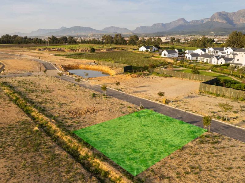 Aerial view of a vacant residential plot in a developed estate, featuring paved road access and scenic mountain views.