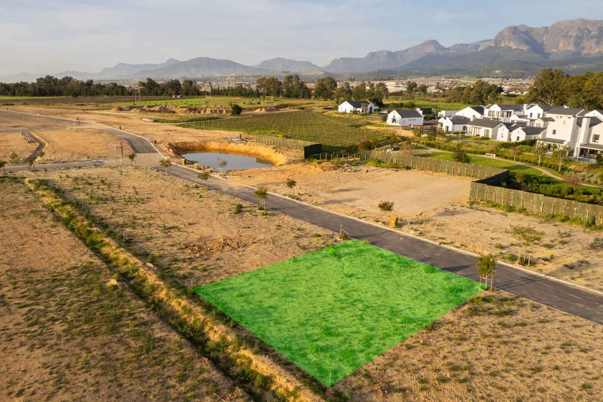 Aerial view of a vacant residential plot in a developed estate, featuring paved road access and scenic mountain views.
