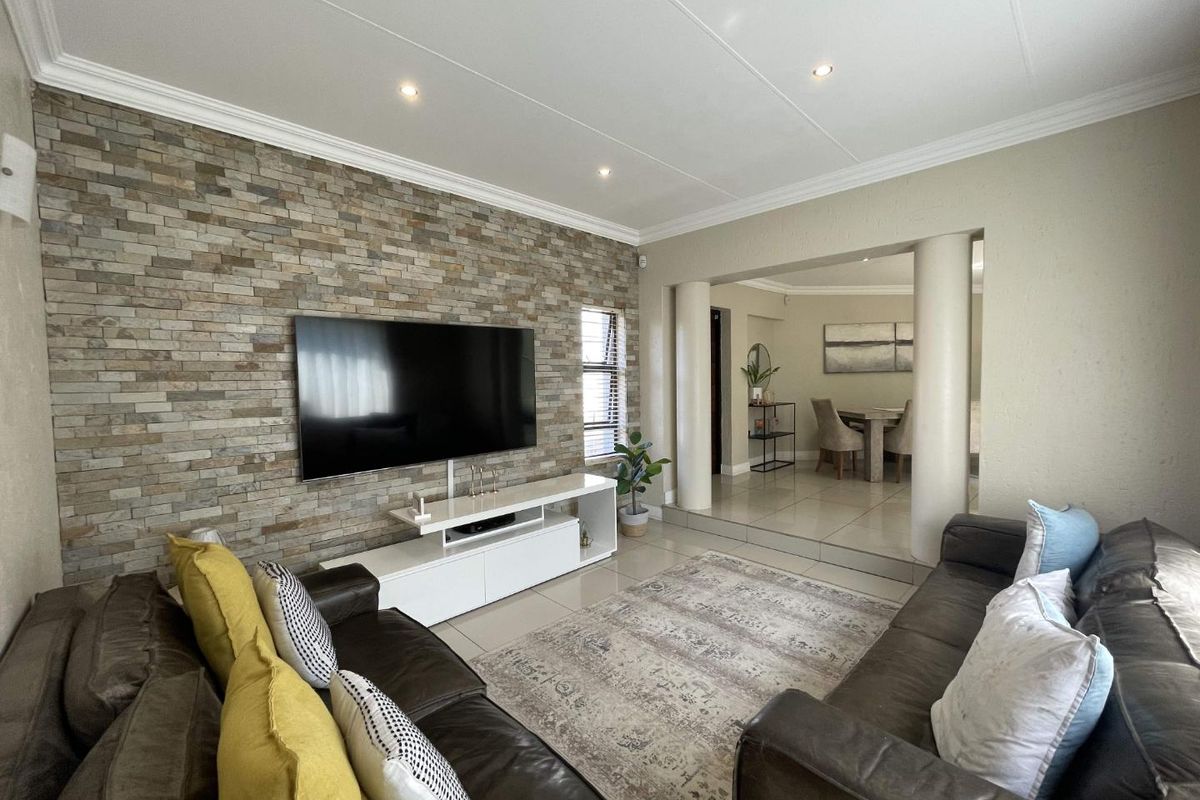 Spacious living room featuring a textured stone accent wall, tiled flooring, and an open-plan layout leading to the dining area.
