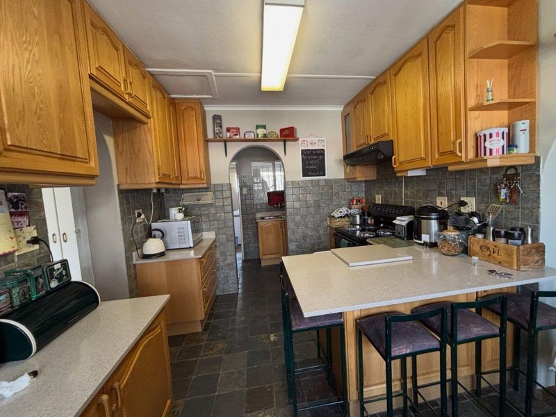 A functional kitchen featuring wooden cabinetry, stone countertops, tiled backsplash, and stone flooring, with an archway leading to an adjacent utility area.