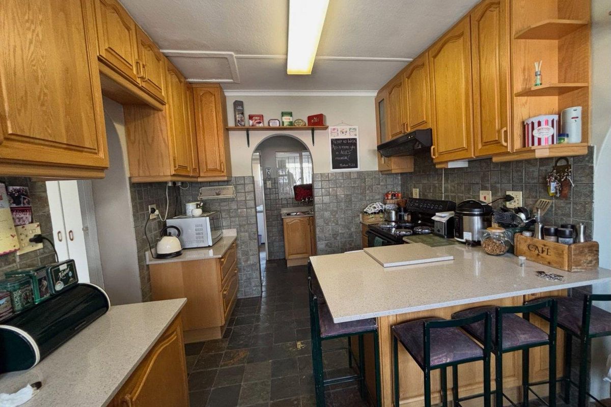 A functional kitchen featuring wooden cabinetry, stone countertops, tiled backsplash, and stone flooring, with an archway leading to an adjacent utility area.