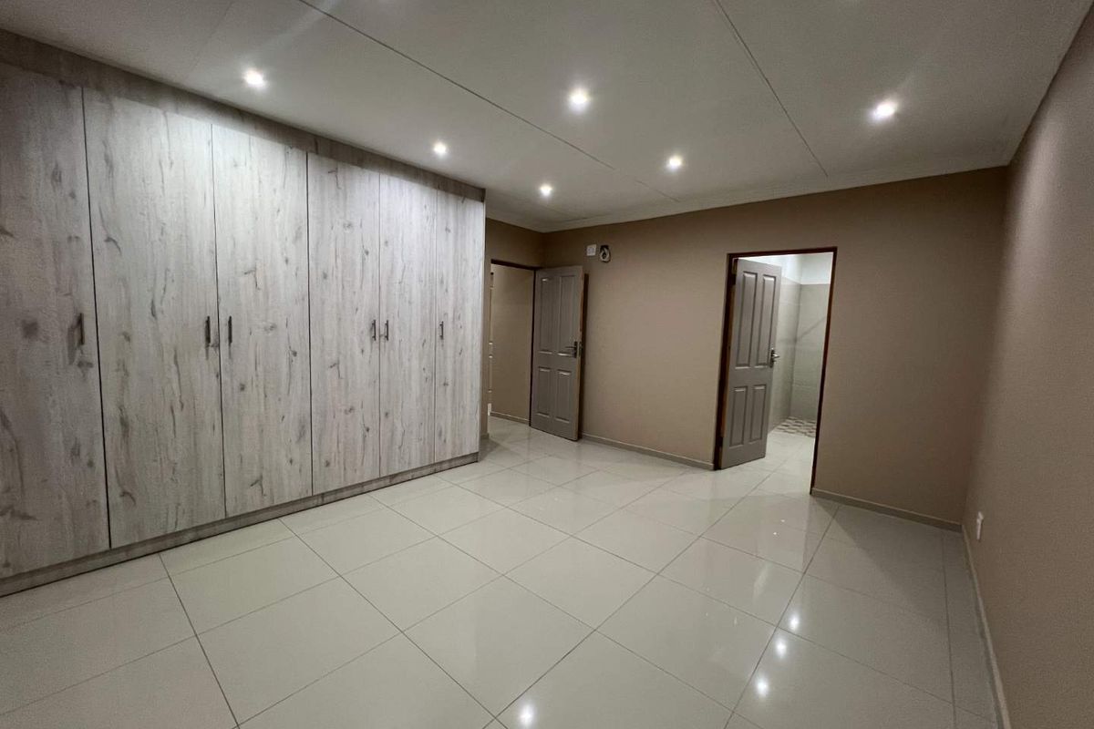 A spacious bedroom featuring neutral tiled flooring, recessed ceiling lighting, and extensive built-in wooden cabinetry for ample storage.