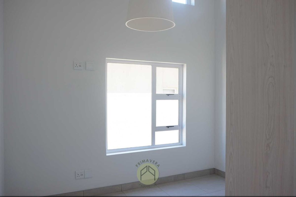 A bright, minimalist bedroom featuring neutral tiled flooring, a modern window, and clean white walls, offering a blank canvas for personalization.
