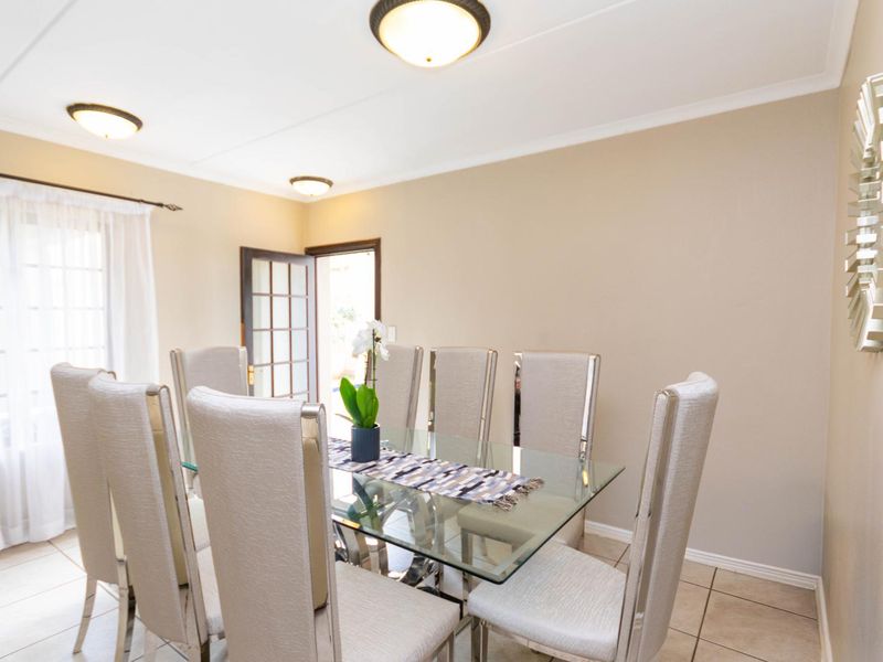 A bright dining room featuring neutral tiled flooring, flush mount lighting, and a glass-paneled door providing access to the exterior.